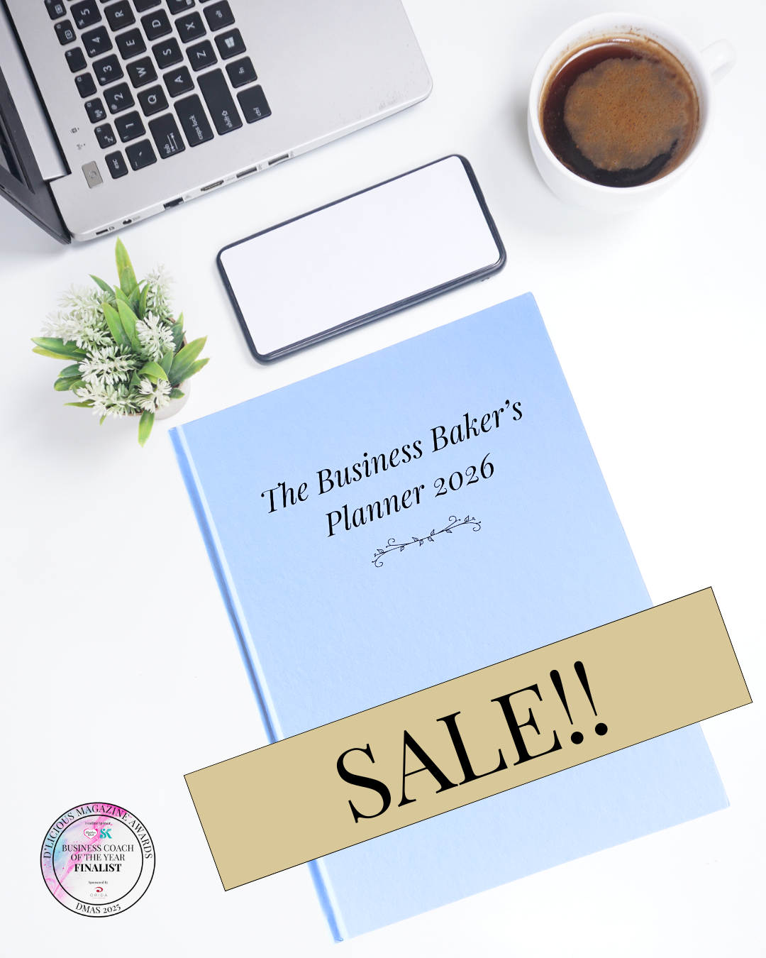Business workspace flatlay with laptop, phone, coffee and plant beside a blue book titled “The Business Baker’s Planner 2026” with a large SALE banner across the cover and award badge in corner.