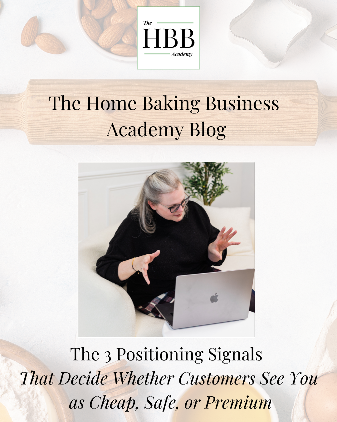 A light, neutral-toned blog header image for The HBB Academy. At the top is the HBB Academy logo in a white box. A rolling pin graphic spans the width of the image with the text 'The Home Baking Business Academy Blog'. Below is a photo of a woman with grey hair and glasses, wearing a black jumper, sitting on a white sofa gesturing with both hands while looking at an open MacBook laptop. Baking ingredients including almonds are visible in the background corners. At the bottom, large text reads 'The 3 Positioning Signals That Decide Whether Customers See You as Cheap, Safe, or Premium'."